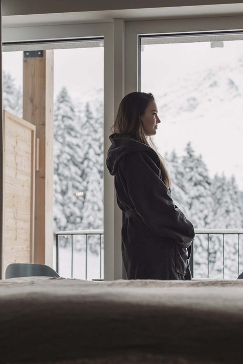 Bilder aus der Sportalm Frau im Bademantel blickt aus Hotelzimmer auf verschneite Berge
