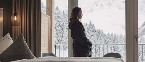 Bilder aus der Sportalm Frau im Bademantel blickt aus Hotelzimmer auf verschneite Berge