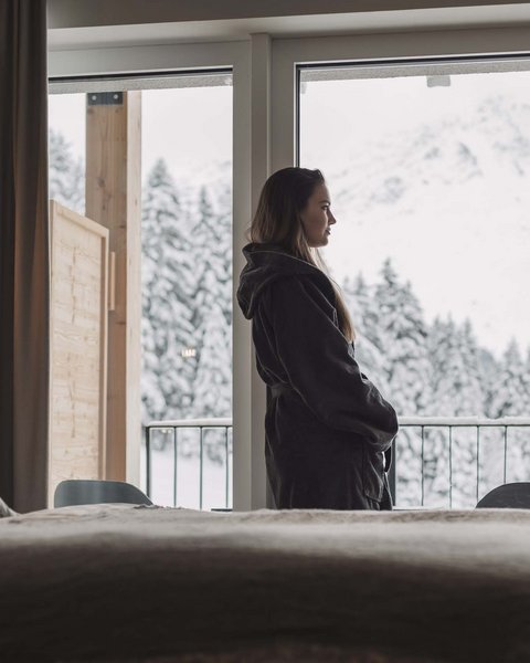 Bilder aus der Sportalm Frau im Bademantel blickt aus Hotelzimmer auf verschneite Berge