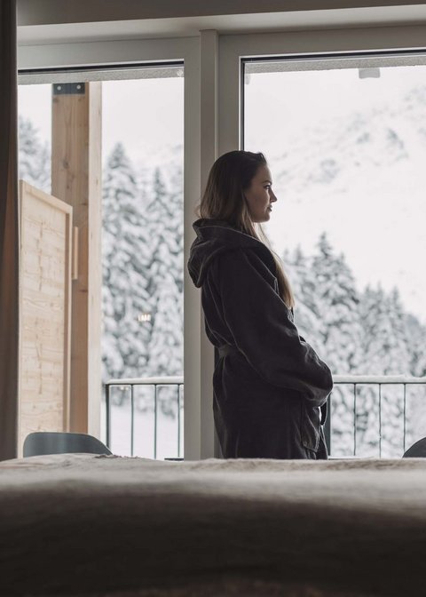 Pictures from Sportalm Woman in robe looking out hotel window at snowy mountain landscape