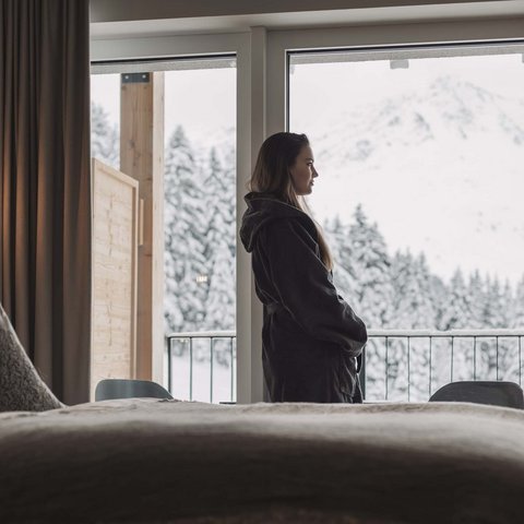 Pictures from Sportalm Woman in robe looking out hotel window at snowy mountain landscape