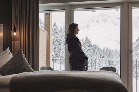 Bilder aus der Sportalm Frau im Bademantel blickt aus Hotelzimmer auf verschneite Berge