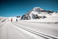 Two cross-country skiers on groomed trail in snowy mountain scenery