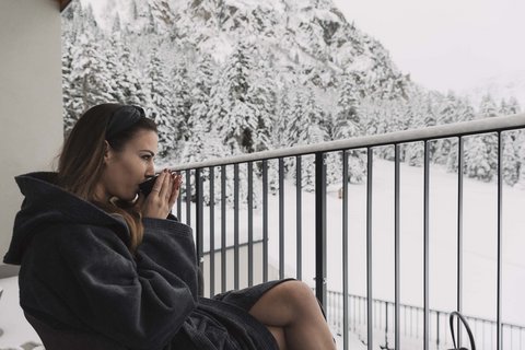 Pictures from Sportalm Woman in bathrobe drinking hot beverage on balcony overlooking snowy mountains