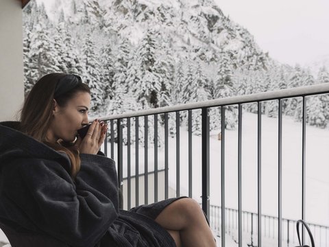 Pictures from Sportalm Woman in bathrobe drinking hot beverage on balcony overlooking snowy mountains