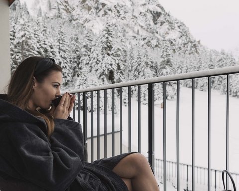 Pictures from Sportalm Woman in bathrobe drinking hot beverage on balcony overlooking snowy mountains