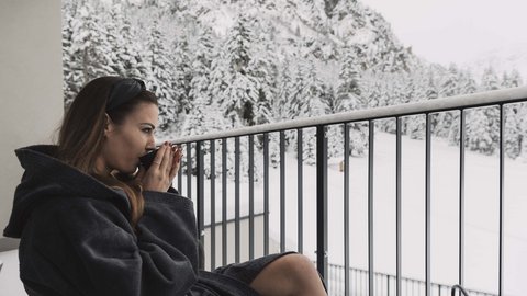 Pictures from Sportalm Woman in bathrobe drinking hot beverage on balcony overlooking snowy mountains