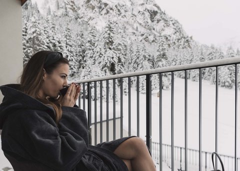 Pictures from Sportalm Woman in bathrobe drinking hot beverage on balcony overlooking snowy mountains