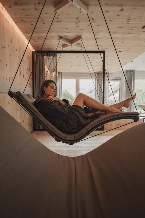 Bilder aus der Sportalm Frau entspannt auf einer hängenden Lounge im modernen Raum mit Holzverkleidung
