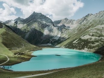 News from Sportalm Clear alpine lake surrounded by tall mountains with hiking trails