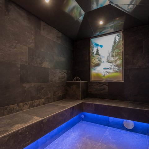 Bilder aus der Sportalm Moderner Wellnessraum mit dunklen Fliesen und blau beleuchtetem Boden