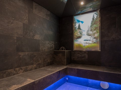 Bilder aus der Sportalm Moderner Wellnessraum mit dunklen Fliesen und blau beleuchtetem Boden