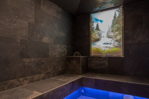 Bilder aus der Sportalm Moderner Wellnessraum mit dunklen Fliesen und blau beleuchtetem Boden