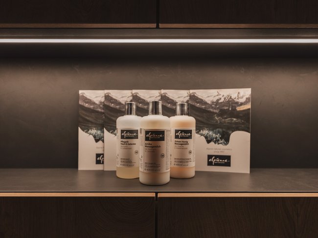 Wohltuende Wellnessbehandlungen Drei Flaschen Alpenkosmetik auf Tisch vor Bergpanorama-Hintergrund