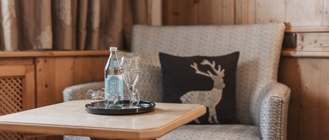 Bilder aus der Sportalm Gemütliche Sitzecke mit Wasserflasche, Gläsern und Hirschkissen auf Holzverkleidung