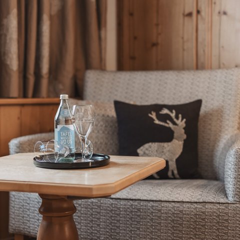 Bilder aus der Sportalm Gemütliche Sitzecke mit Wasserflasche, Gläsern und Hirschkissen auf Holzverkleidung