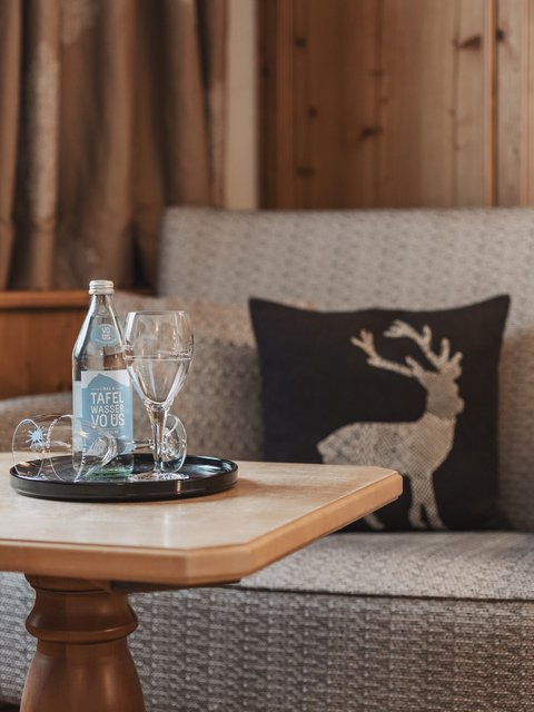 Bilder aus der Sportalm Gemütliche Sitzecke mit Wasserflasche, Gläsern und Hirschkissen auf Holzverkleidung