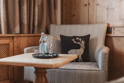 Bilder aus der Sportalm Gemütliche Sitzecke mit Wasserflasche, Gläsern und Hirschkissen auf Holzverkleidung