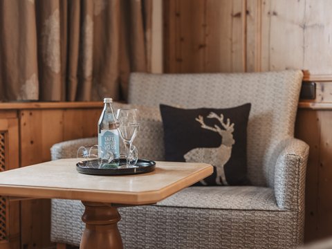 Bilder aus der Sportalm Gemütliche Sitzecke mit Wasserflasche, Gläsern und Hirschkissen auf Holzverkleidung