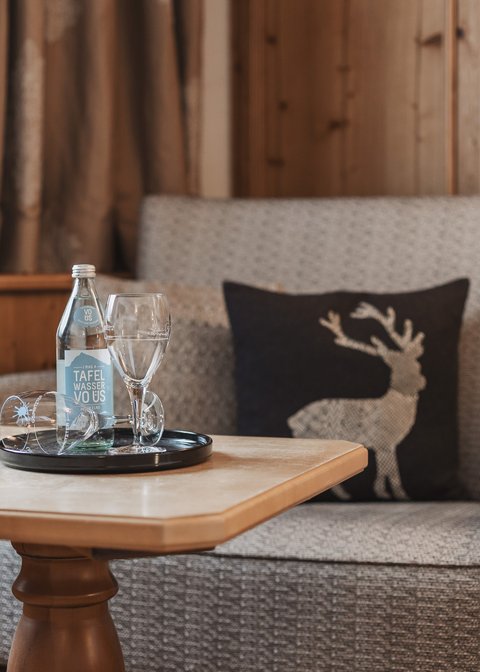 Bilder aus der Sportalm Gemütliche Sitzecke mit Wasserflasche, Gläsern und Hirschkissen auf Holzverkleidung