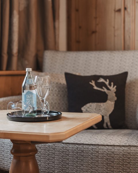 Bilder aus der Sportalm Gemütliche Sitzecke mit Wasserflasche, Gläsern und Hirschkissen auf Holzverkleidung