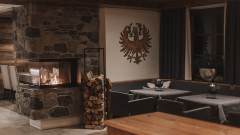 Bilder aus der Sportalm Gemütlicher Raum mit Steinofen, Holzstapel und verzierten Wänden