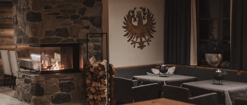 Bilder aus der Sportalm Gemütlicher Raum mit Steinofen, Holzstapel und verzierten Wänden