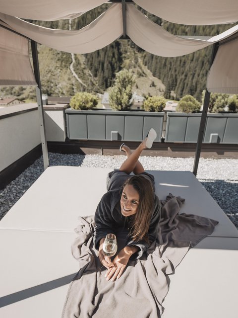Pictures from Sportalm Woman lying on terrace bed under canopy holding a glass of wine