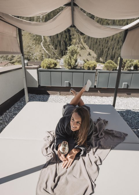 Bilder aus der Sportalm Frau liegt auf Terrasse unter Sonnenschutz mit Glas Wein in der Hand