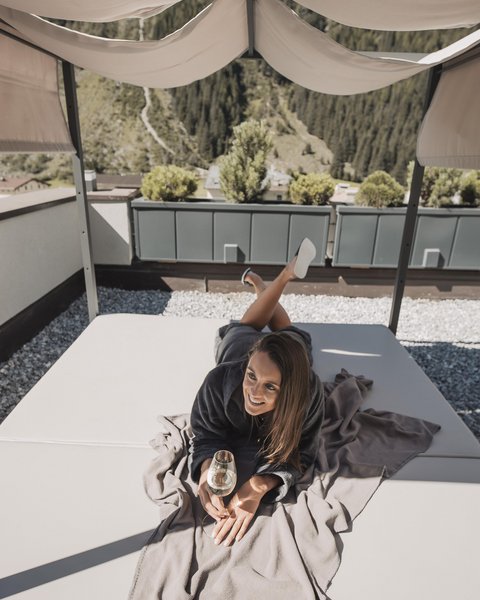 Bilder aus der Sportalm Frau liegt auf Terrasse unter Sonnenschutz mit Glas Wein in der Hand