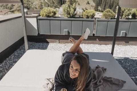 Bilder aus der Sportalm Frau liegt auf Terrasse unter Sonnenschutz mit Glas Wein in der Hand