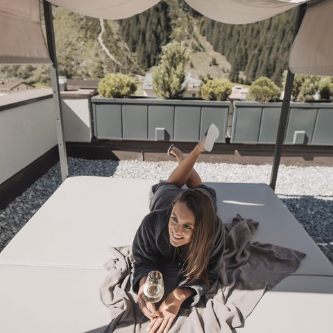 Pictures from Sportalm Woman lying on terrace bed under canopy holding a glass of wine