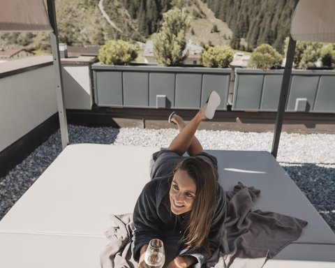 Pictures from Sportalm Woman lying on terrace bed under canopy holding a glass of wine