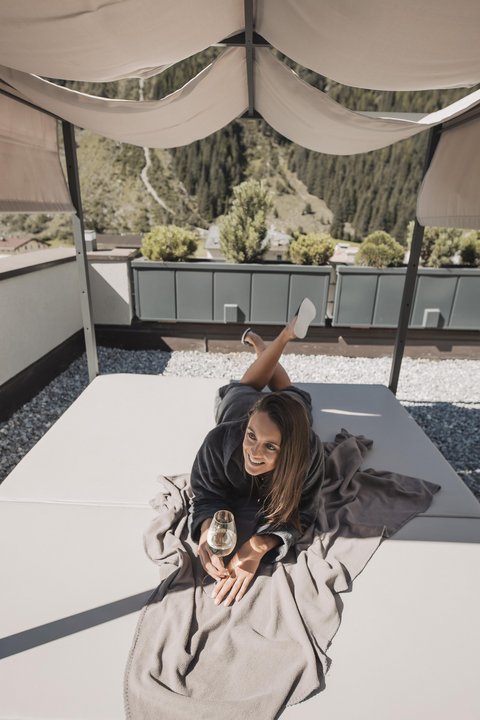 Pictures from Sportalm Woman lying on terrace bed under canopy holding a glass of wine