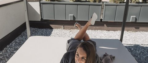 Bilder aus der Sportalm Frau liegt auf Terrasse unter Sonnenschutz mit Glas Wein in der Hand