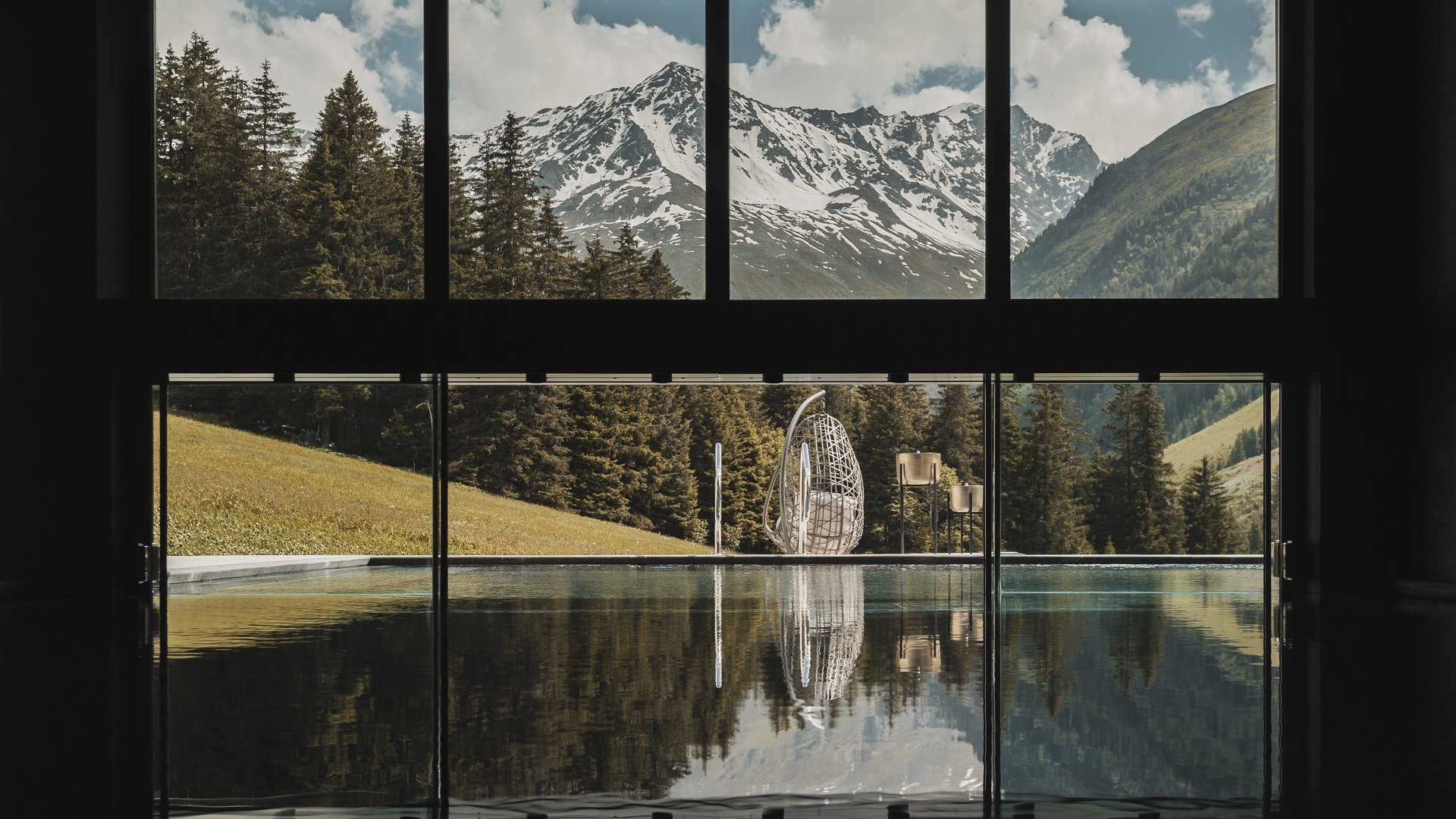 Urlaub im Pitztal? Unterkunft mit Pep! Blick auf verschneite Berge und Bäume durch große Fenster mit reflektierendem Pool