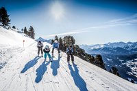 Four skiers skiing down snowy slope with mountains in the background