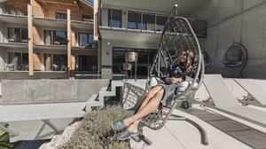 Hiking hotel in Pitztal: nature adventurers, ahoy! Woman relaxing in hanging chair on hotel terrace in sunny weather